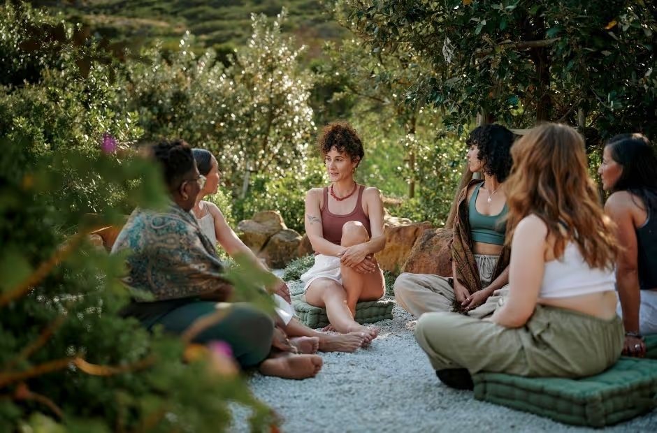 Grupo de mulheres sentadas em roda ao ar livre, em meio à natureza