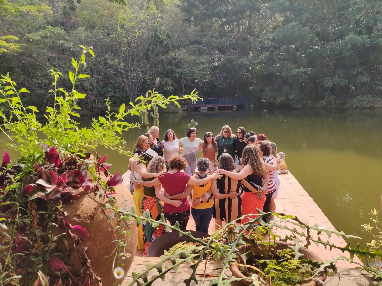 Mulheres abraçadas em círculo em um deck à beira do lago